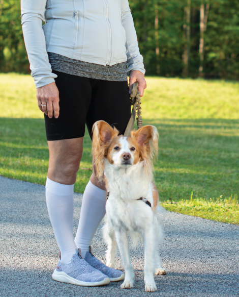 Woman wearing Sigvaris Essential Cotton compression socks, standing in a park with a Papillon dog