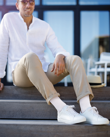 Man lounging on patio steps in casual attire and Sigvaris Motion Cushioned Cotton compression socks in the color White